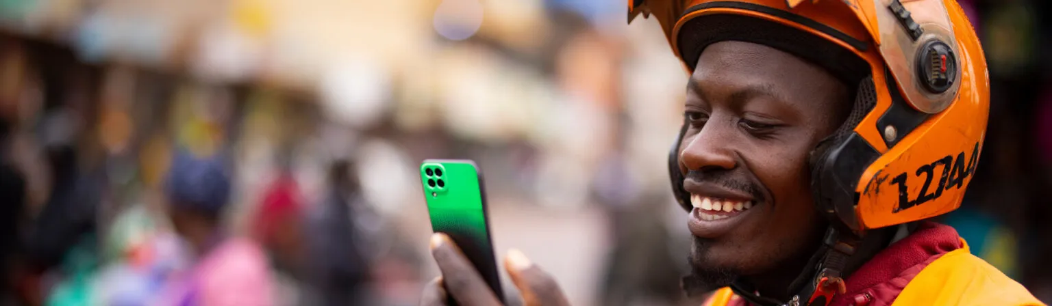 A boda-boda rider checking his phone on a busy street